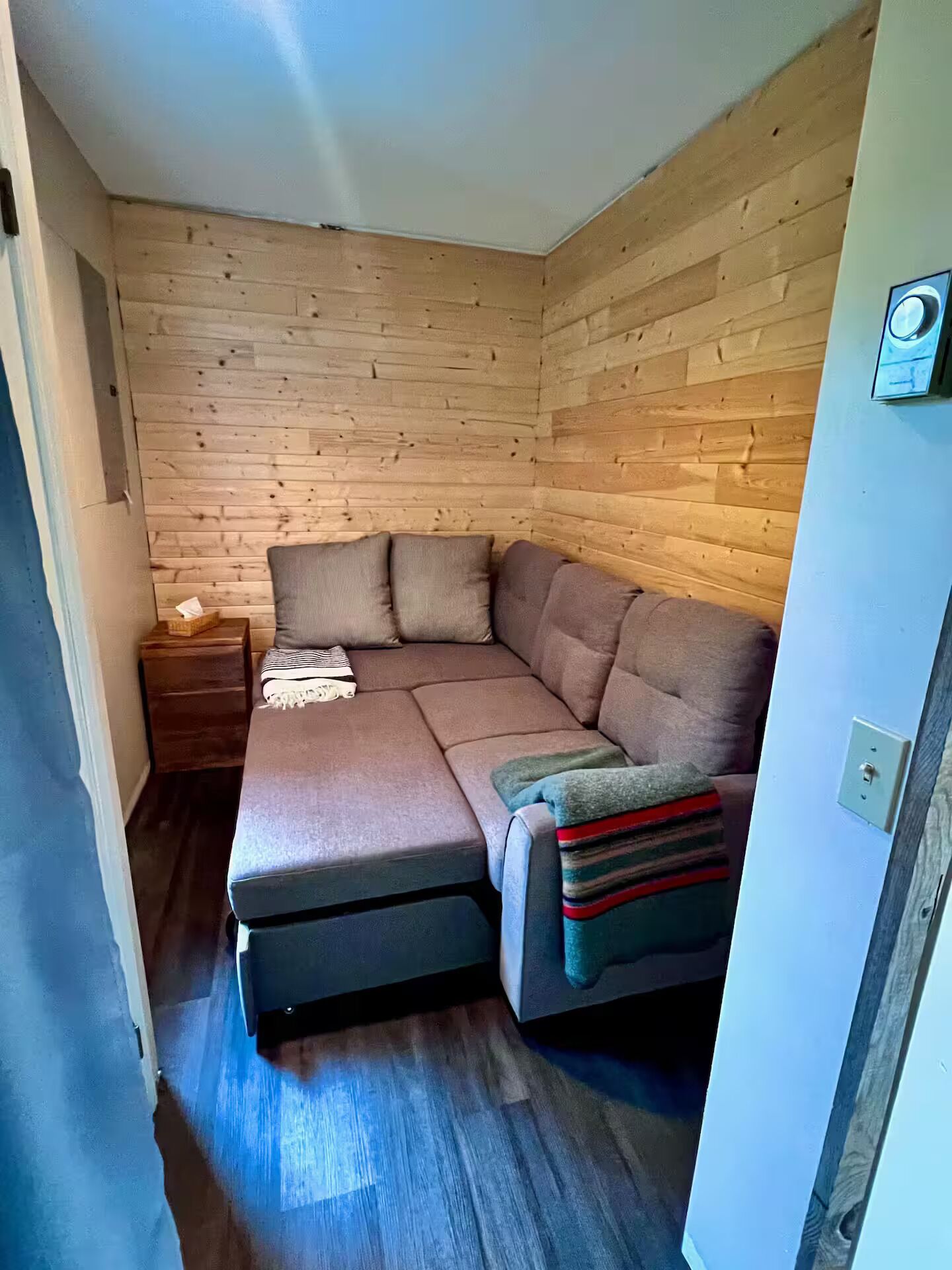 Une petite pièce d’angle avec un mur en bois, un canapé et une petite table de chevet.