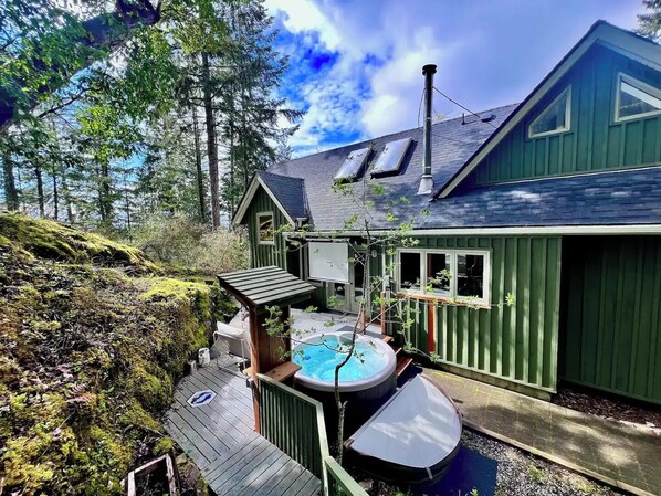 A green cabin with a hot tub and a deck.