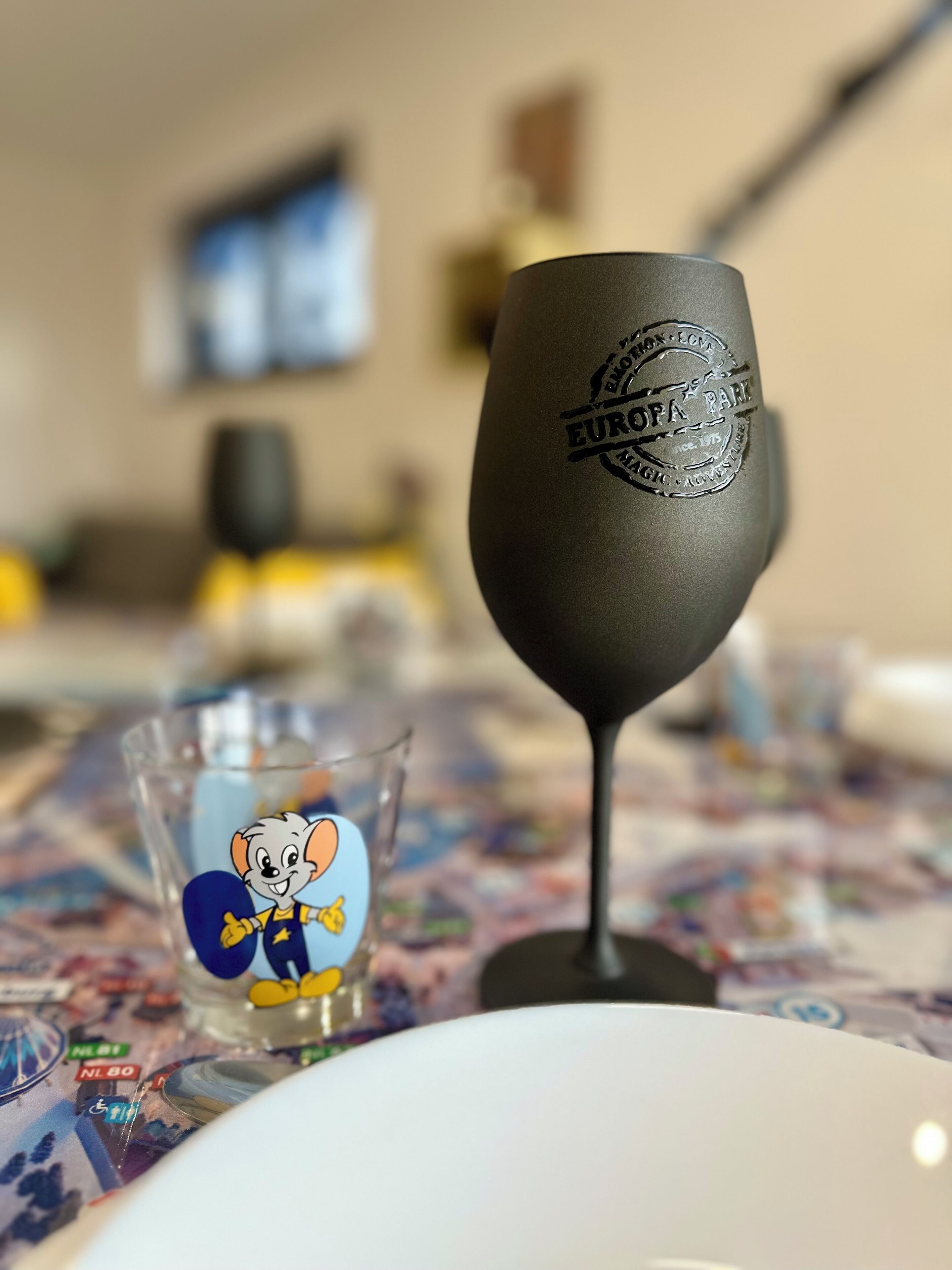 Una copa de vino con un logotipo sobre una mesa con mantel colorido.