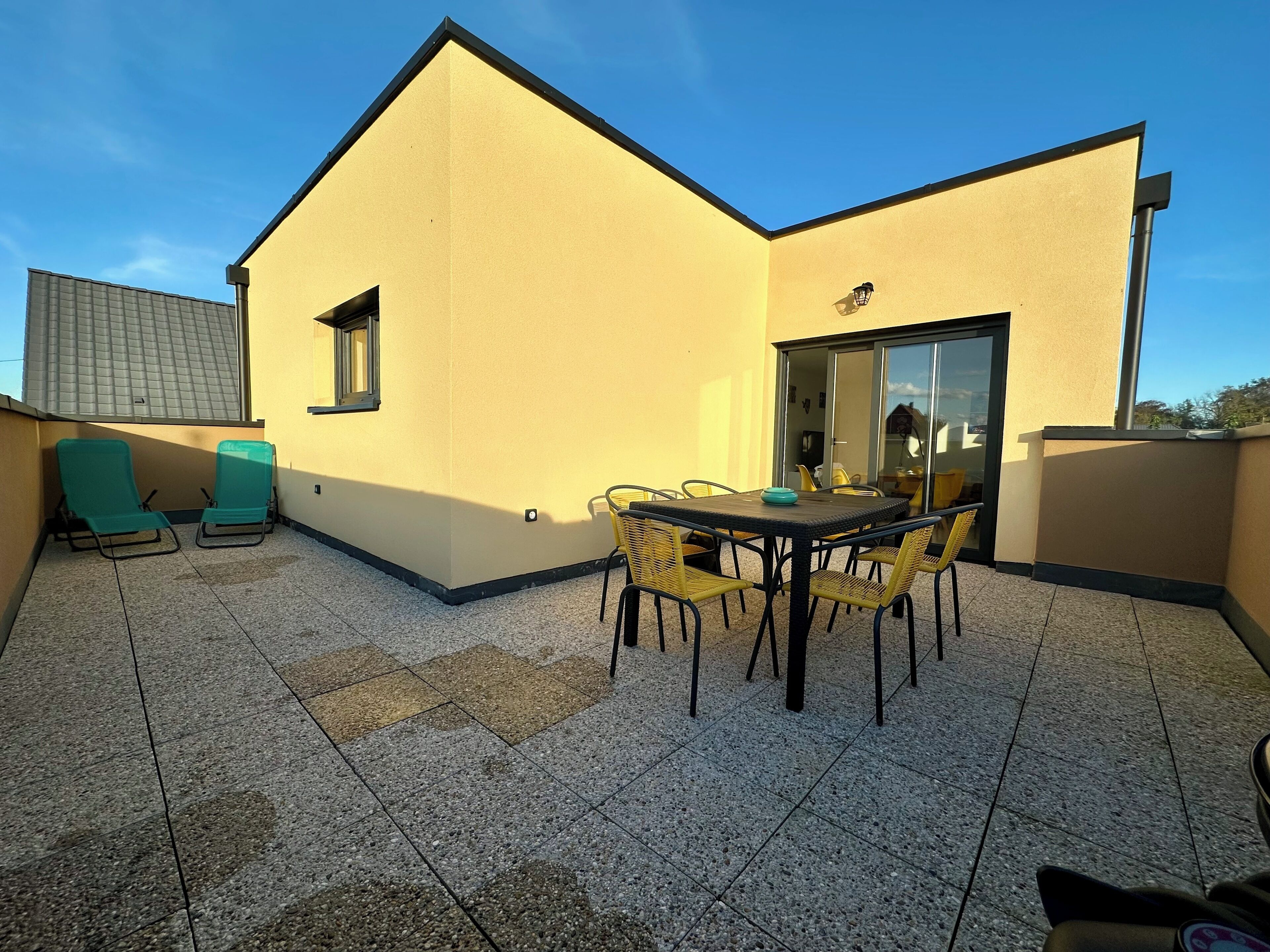 A rooftop terrace with a table and chairs, a small window, and a door leading to an interior space.