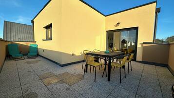 A rooftop terrace with a table and chairs, a small window, and a door leading to an interior space.