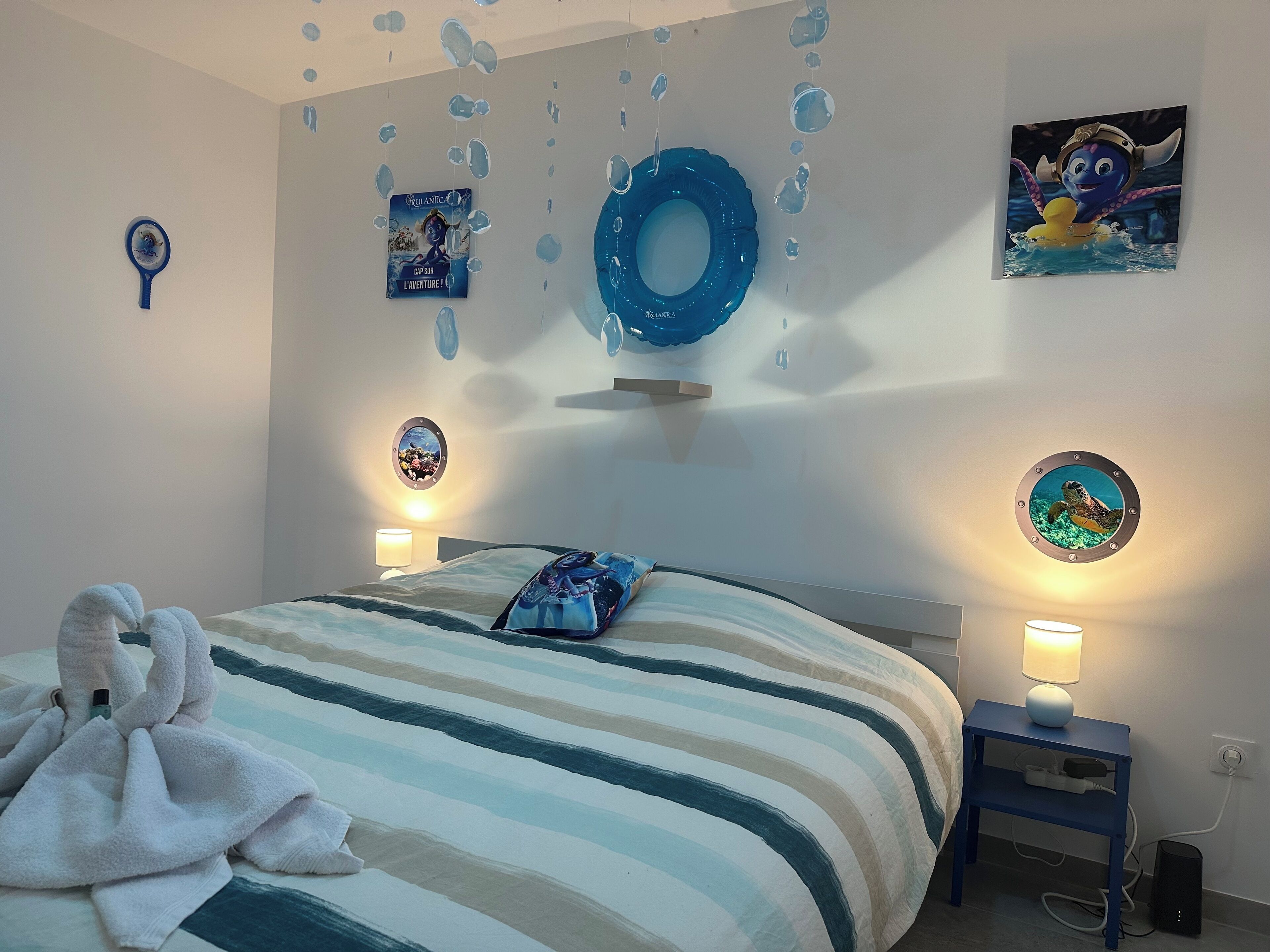 Een slaapkamer met een gestreepte spreidek, een blauwe, ronde decoratie aan de muur en een lijst met een afbeelding van een zeedier.