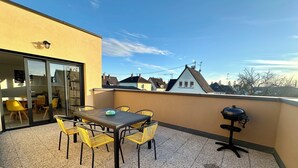 A balcony with a table and chairs, a grill, and a view of neighboring houses. - Europ-Appart ~ {Europa-Park / Rulantica} (Huttenheim)