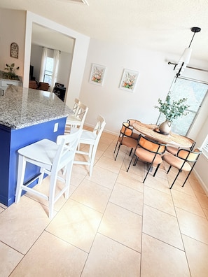 A kitchen with a granite countertop, white chairs, a dining table, and a potted plant.