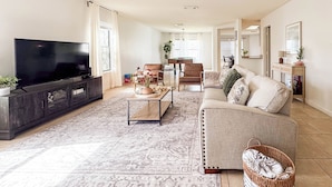 A living room with a flat-screen TV, a sofa, a coffee table, and a patterned rug. - Cosina. equipped. 6 beds 3 large baths. spaces.  (Live Oak)