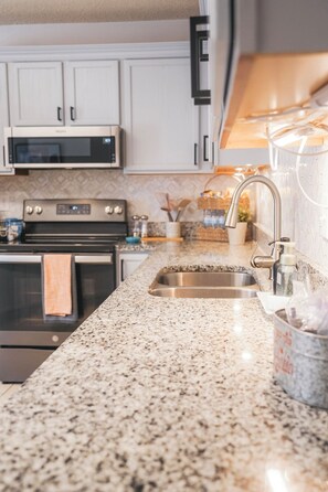 A kitchen with white cabinets, a stainless steel microwave, a gas stove, and a granite countertop.