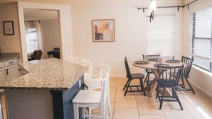 A modern kitchen with a granite countertop, white chairs, a dining table with black chairs, a hanging light fixture, and a framed artwork on the wall. - Cosina. equipped. 6 beds 3 large baths. spaces.  (Live Oak)