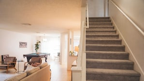 A living room with a beige sofa, a pool table, and a staircase. - Cosina. equipped. 6 beds 3 large baths. spaces.  (Live Oak)