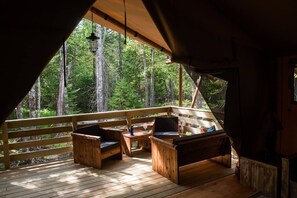 Een houten terras met twee houten stoelen en een tafel, met uitzicht op een bos.