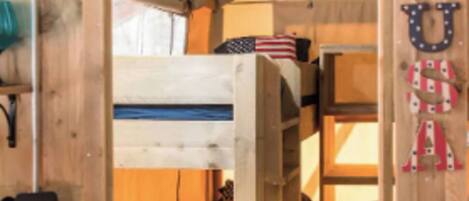 Een houten interieur met stapelbedden, een bureau en een stoel, en een aan de muur bevestigde Amerikaanse vlag.