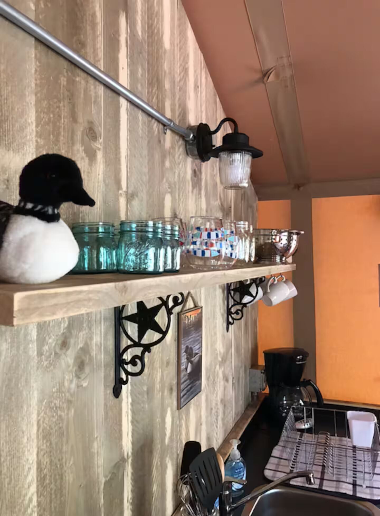 Une cuisine rustique avec un mur en bois, une étagère remplie de bocaux, une décoration représentant un canard et une machine à café.