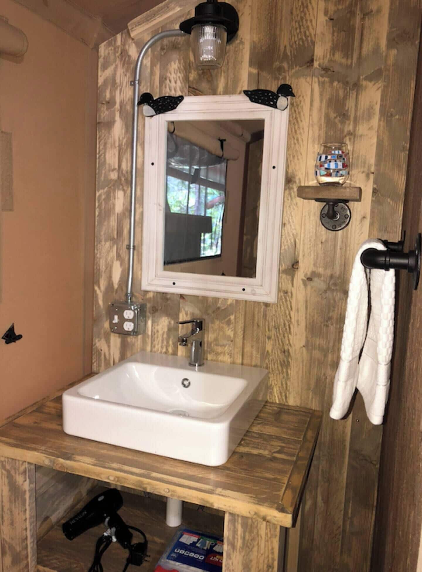 A bathroom with a wooden wall, a white sink, a mirror, and a towel rack.