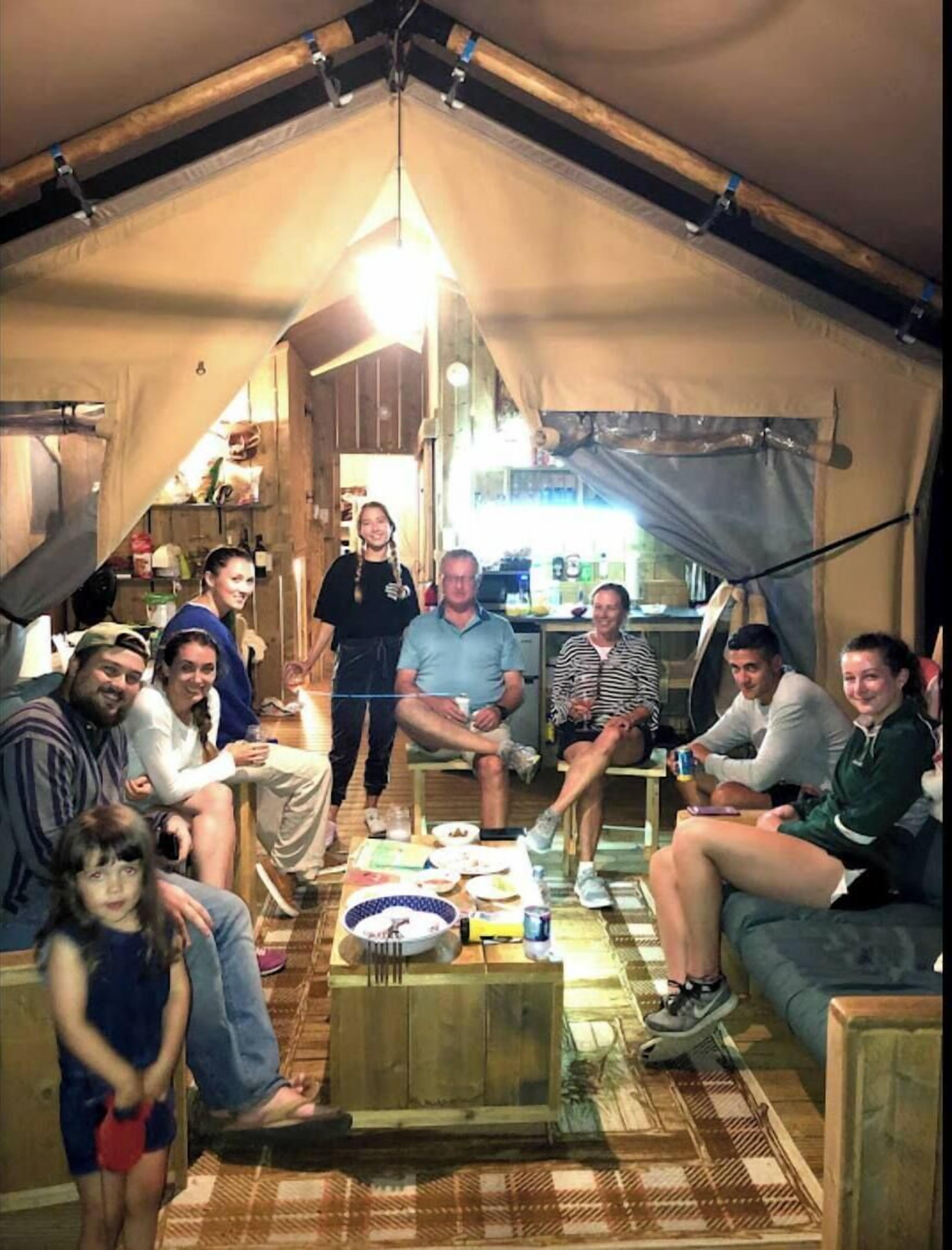 Un groupe de personnes se trouve dans un hébergement sous tente, avec une table à manger placée au centre.