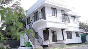 A two-story white building with a balcony on the upper floor, a staircase leading to the entrance, and a small porch area. - Wind Castle (Kanayannur)