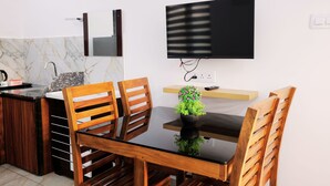 A modern kitchen with a marble backsplash, wooden chairs, a black table, and a flat-screen TV mounted on the wall. - Wind Castle (Kanayannur)