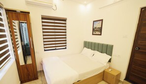 Makuuhuone, jossa on sänky, yöpöytä, ikkuna, jossa on sälekaihtimet, ovi ja seinälle ripustettu taulu.