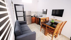 A compact living space with a kitchenette, a dining area with wooden chairs, a sofa, and a flat-screen TV mounted on the wall. - Wind Castle (Kanayannur)