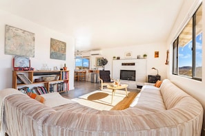 Uma sala de estar ampla com um sofá grande, lareira, estante de livros e área de jantar.