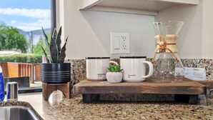 Een keukentafel met een koffiezetapparaat, een glazen kan en een bloempot.
