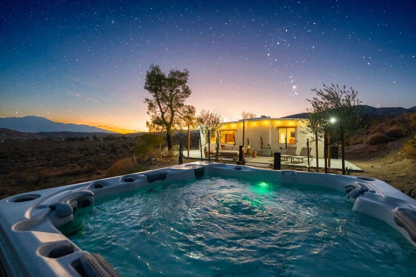 Een bubbelbad met een zwembadgedeelte, een huis met terras en een sterrenhemel.