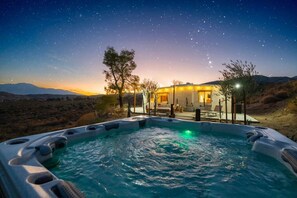 Un jacuzzi con zona de piscina, una casa con patio y un cielo nocturno estrellado.