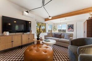 A living room with a large flat-screen TV, a sofa, a coffee table, and a patterned floor. - Palo Verde Casa | Spa | Joshua Tree + Palm Springs (Morongo Valley)