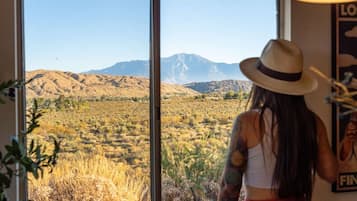 A room with large windows offering a view of a desert landscape with mountains.