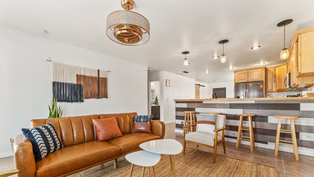 A modern living room with a leather sofa, a coffee table, and a bar area with stools. - The Farm House | Pool&Spa | 5 min to JT Park (Twentynine Palms)
