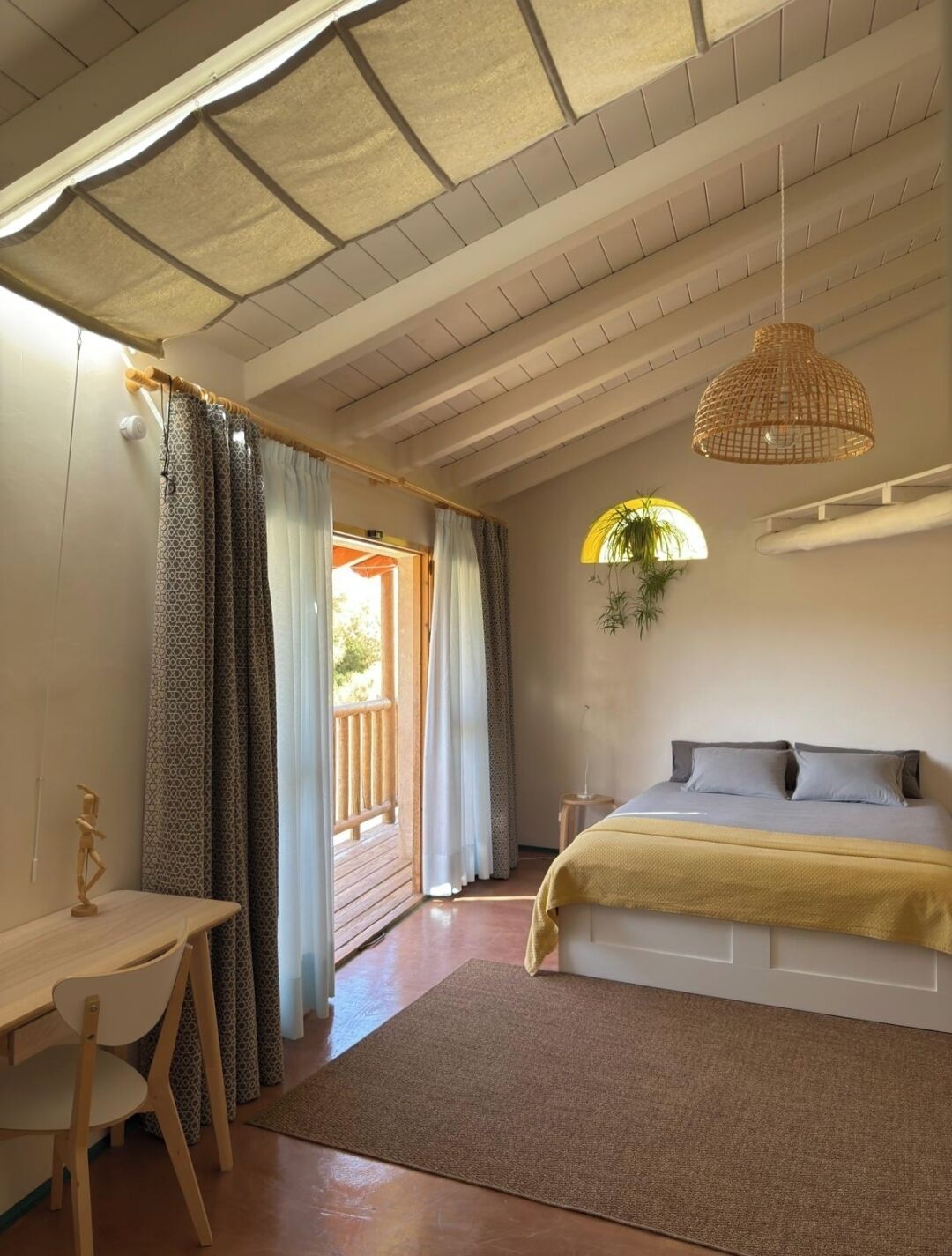 A bedroom with a bed, a desk, and a hanging light fixture.
