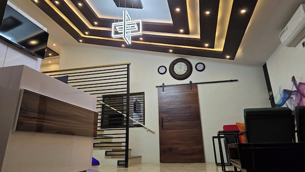 A modern interior with a staircase, a wooden door, and a ceiling with recessed lighting and a geometric light fixture. - NEKST Hotel (Ibadan)