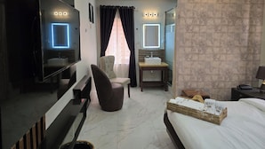 A modern hotel room with a large bed, a TV, a desk with a chair, a bathroom with a sink and mirror, and a wall-mounted air conditioner. - NEKST Hotel (Ibadan)