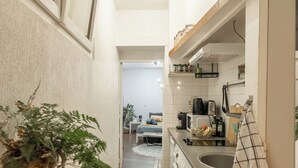 A narrow hallway leading to a kitchen with a washing machine, a sink, and a countertop with various items.