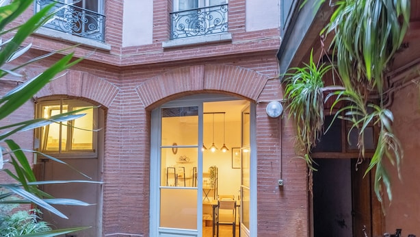 A courtyard with a brick building, a wooden door, and potted plants.