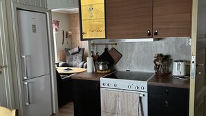 A compact kitchen with a refrigerator, stove, and wooden cabinets. - Sørøya: Skipper view Akkarfjord, 210m from pub, diner and quay. Sørøya along the coast! (Finnmark)