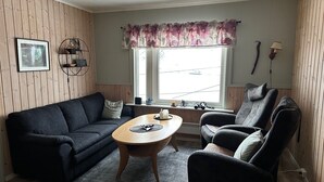 A cozy living room with a dark sofa, a wooden coffee table, and a patterned rug. - Sørøya: Skipper view Akkarfjord, 210m from pub, diner and quay. Sørøya along the coast! (Finnmark)