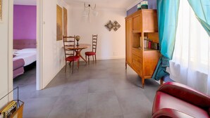 A hotel room with a bed, a dining area with a table and chairs, a wooden cabinet, and a view of another room. - mimi terrace (Naples)