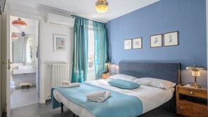 A bedroom with a bed, a nightstand, a bedside lamp, a window with curtains, a wall with framed pictures, and a bathroom visible through an open door. - mimi terrace (Naples)