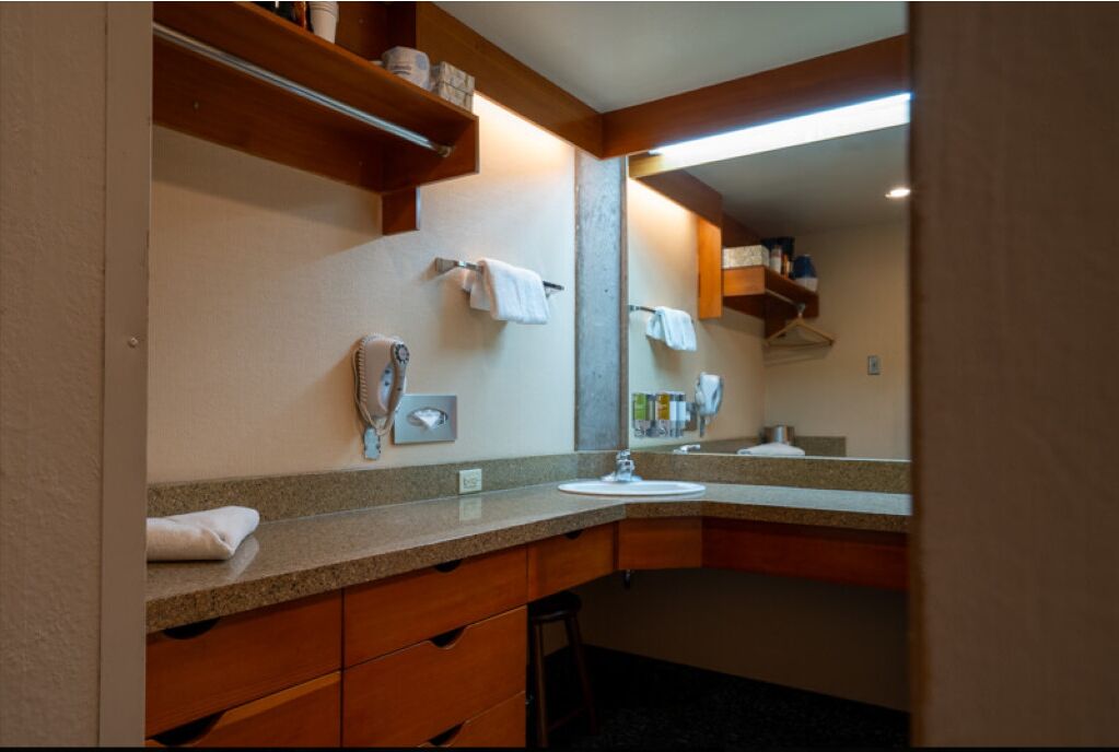 Un baño con encimera de granito, lavamanos, espejo y muebles de madera.