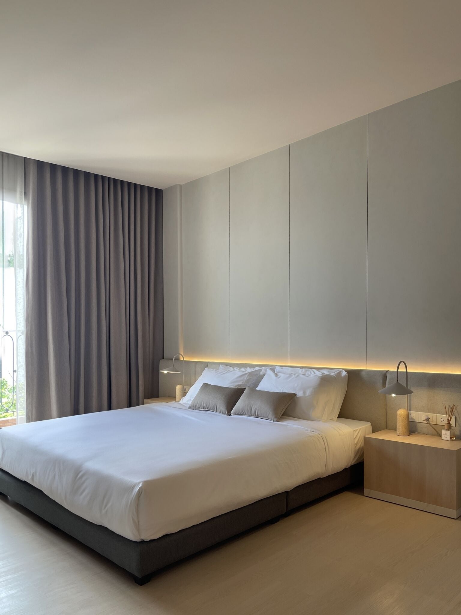 A modern bedroom with a large bed, grey curtains, and bedside lamps.