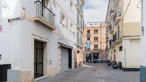 A narrow cobblestone street flanked by multi-story buildings with balconies, a closed shop, and parked motorcycles. - MARA ARENAL. AMPLIO APARTAMENTO EN EL CENTRO DE SEVILLA IDEAL PARA FAMILIAS (Sevilla)