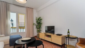 A modern living room with a sofa, a small table, a TV on a wooden cabinet, a potted plant, and a wine bottle on a side table. - MARA ARENAL. AMPLIO APARTAMENTO EN EL CENTRO DE SEVILLA IDEAL PARA FAMILIAS (Sevilla)