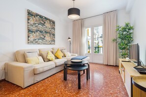 Ein Wohnzimmer mit einer Couch, einem Couchtisch, einer Lampe, einem Fernseher und einer großen Pflanze.