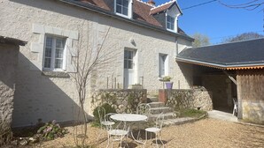 A stone house with a tiled roof, a small garden with a table and chairs, and a stone wall. - Gîte in the heart of the Loire castles (Athée-sur-Cher)