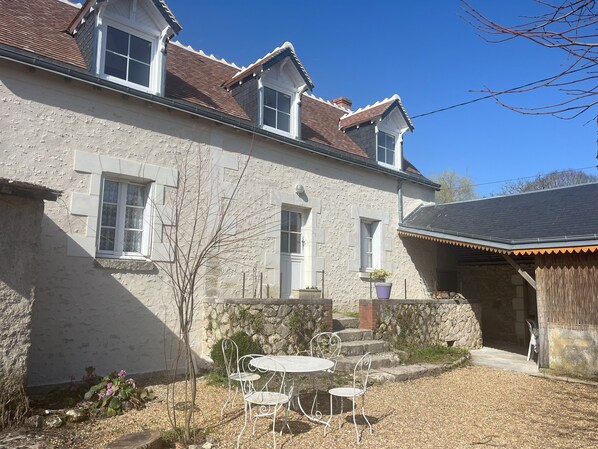 A stone house with a tiled roof, a small garden with a table and chairs, and a stone wall.
