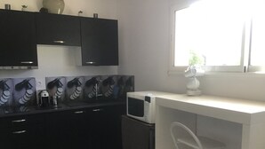 A kitchen with black cabinets, a microwave, a coffee maker, and a window with a view of greenery. - Apartment in a haven of peace 10 mm from the Mediterranean Sea. (Sorède)