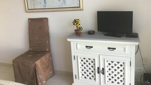 A room with a white cabinet, a television on top, and a framed abstract painting on the wall. - Apartment in a haven of peace 10 mm from the Mediterranean Sea. (Sorède)