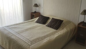 A neatly made bed with a patterned bedspread and two pillows, a bedside table with a lamp, and a wardrobe against the wall. - Apartment in a haven of peace 10 mm from the Mediterranean Sea. (Sorède)