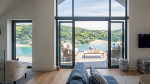 A spacious living room with a large sliding glass door leading to a deck overlooking a beach and hills.