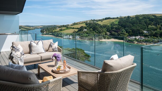 A balcony with a sofa, wicker chairs, and a table with a bottle and flowers.