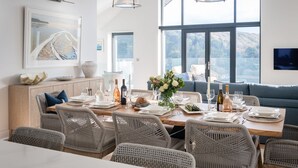 A dining area with wicker chairs, a wooden table set for a meal, and a large window offering a view of the outdoors.